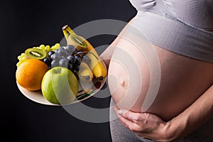 A pregnant woman with belly holding a plate with fruits. Concept for weight control and healthy eating during pregnancy