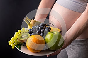 A pregnant woman with belly holding a plate with fruits. Concept for weight control and healthy eating during pregnancy