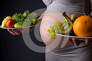 Pregnant woman with belly holding a plate with fruits and vegetables in hands. Concept healthy eating during pregnancy