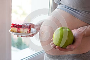 Pregnant woman belly holding a plate with junk and healthy food. Concept choice of diet during pregnancy