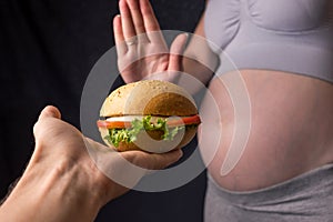Pregnant woman with belly refuses from the burger. The concept control during pregnancy weight