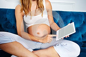 Pregnant woman belly show reading ebook on a sofa