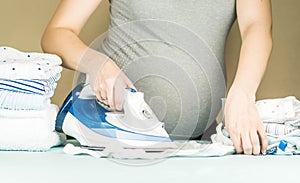 Pregnant woman with big belly preparing, ironing newborn baby clothes before labor