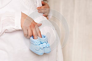 pregnant woman with a big belly, tummy, holding knitted shoes for the baby