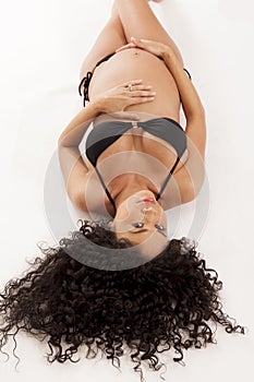 Pregnant woman in a bikini lying on the ground.