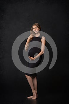 Pregnant woman on black background with big tummy, waiting for baby.