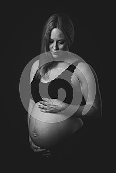 Pregnant woman in black underwear  holding belly on black background