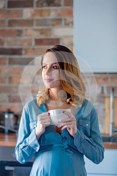 Pregnant woman in blue clothes with cup of tea or coffee