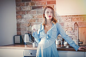 Pregnant woman in blue dress with cup of coffee or tea