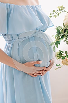 Pregnant woman in blue dress holds hands on belly on a white background. Pregnancy, maternity, preparation, expectation concept.