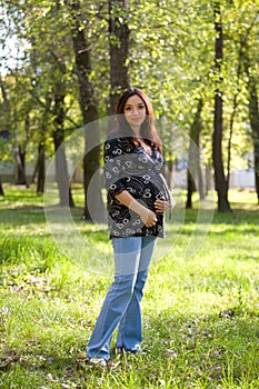 Pregnant woman in blue jeans saunter in park