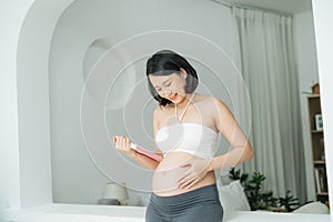 Pregnant woman with book. Cheerful young pregnant woman touching her abdomen and reading book while standing isolated on white