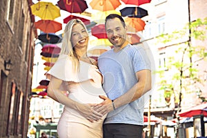 Pregnant woman with boyfriend on city street with umbrella on the background