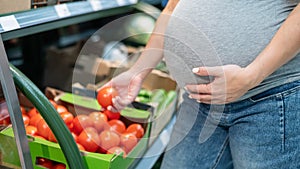 Pregnant woman buys tomatoes in the store.
