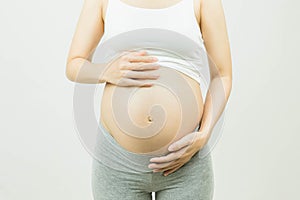 Pregnant woman caressing her belly over gray background-Motherhood, pregnancy, people and expectation concept