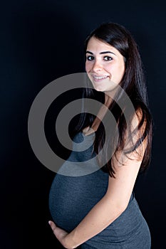 Pregnant woman caressing her belly under black background