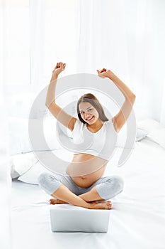 Pregnant Woman Celebrates Something. Happy Woman using Laptop Co