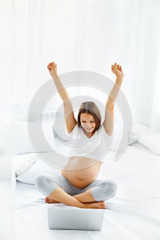 Pregnant Woman Celebrates Something. Happy Woman using Laptop Co