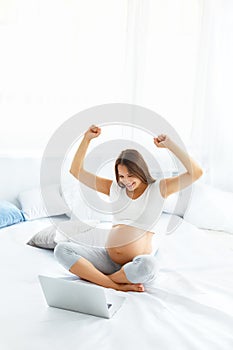 Pregnant Woman Celebrates Something. Happy Woman using Laptop Co