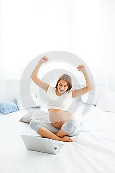 Pregnant Woman Celebrates Something. Happy Woman using Laptop Co