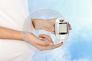 Pregnant woman checking blood sugar level with glucometer on color background. Diabetes test