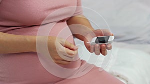 Pregnant woman checking blood sugar level by herself with glucose meter at home. gestational diabetes concept