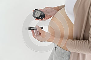 Pregnant woman checking blood sugar level by using Digital Glucose meter, health care, medicine, diabetes, glycemia concept