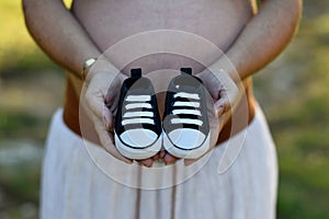 Pregnant woman with child shoes in hands and on top of tummy photo