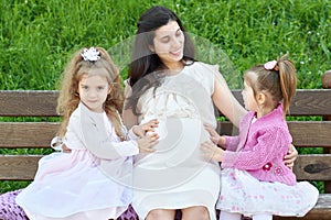 Pregnant woman and children in summer city park outdoor, happy family, bright sunny day and green grass, beautiful people portrait