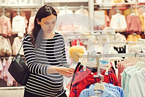 Pregnant woman chooses clothes for her future daughter. Mother doing shopping in baby shop