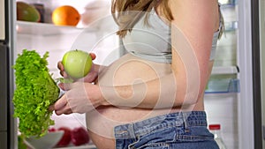 Pregnant woman chooses green apple salad and vegetables. Vegetarian food in fridge during pregnancy. Close-up shot of