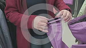 Pregnant woman chooses purple windbreaker jacket with rain hood in store to buy