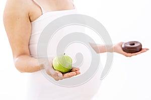 Pregnant woman choosing healthy apple over unhealthy donut