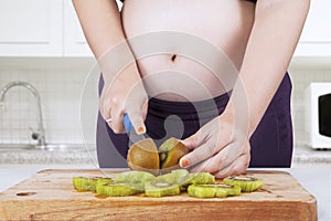 Pregnant woman chopping kiwi fruit