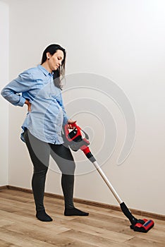 Pregnant woman cleaning floor with handheld vacuum cleaner. Young pregnant woman enjoys cleaning her house