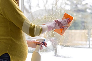 Pregnant woman cleaning window with cloth and window spray. Sping cleaning concept