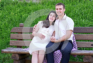 Pregnant woman closed eyes and dreaming, and husband on outdoor, happy family, couple in city park, summer season, green grass and