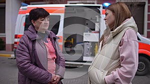 Pregnant woman communicating with paramedic near ambulance.