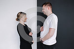 Pregnant woman compare her belly to her husband's beer belly on black and white background