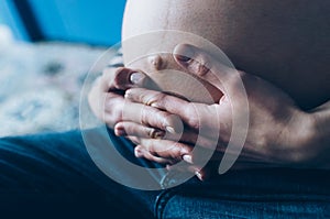 Pregnant woman cuddling belly in bedroom at home just before the labor and childbirth, selective focus