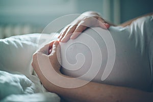 Pregnant woman cuddling belly in bedroom at home