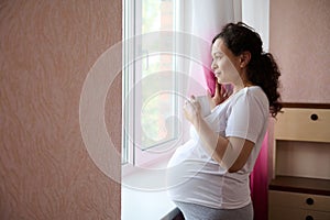 Pregnant woman with cup of healthy tea, looking dreamily out the window, enjoying her pregnancy and maternity lifestyle