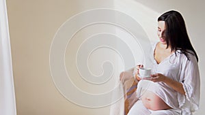 A pregnant woman with a cup of tea looks out the window