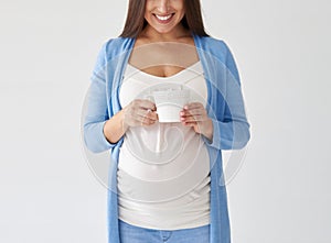 Pregnant woman with cup of tea posing against white background i