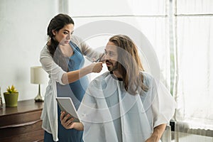 The pregnant woman is cutting her husband. Bearded man getting haircut by his wife at home new normal concept