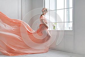 Pregnant woman dancing in pink evening dress flying on wind. Waving fabric, fashion shot.