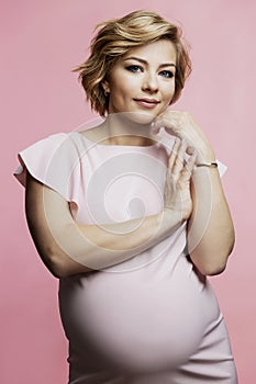 Pregnant woman in a delicate dress. Beautiful smiling blonde with a big belly on a pink background. Waiting for the birth of a