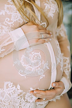 A pregnant woman in a delicate pink lace pinewear holds her belly with her hands
