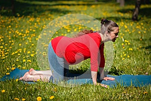 Pregnant woman doing asana Bitilasana outdoors