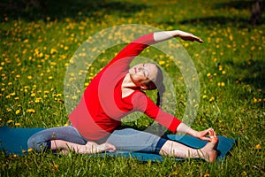 Pregnant woman doing asana Parivrtta Janu Sirsasana outdoors